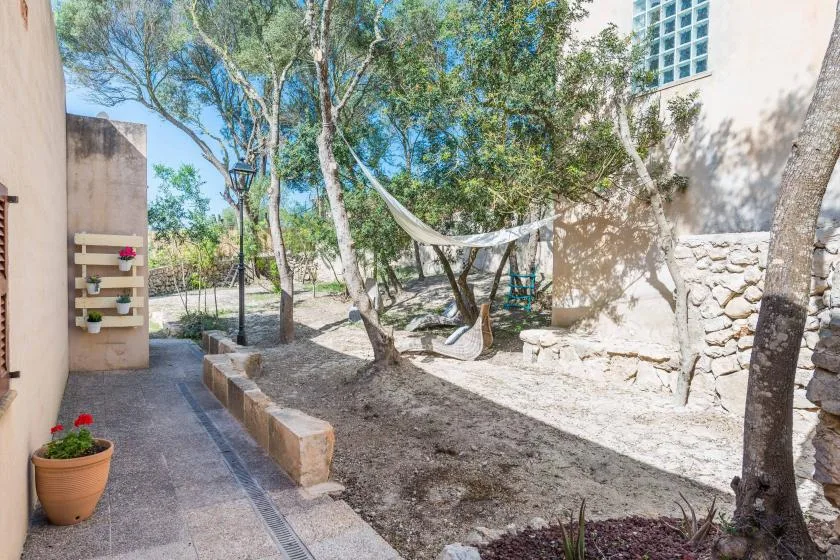 Un patio exterior sombreado con árboles, una hamaca y un sendero pavimentado.