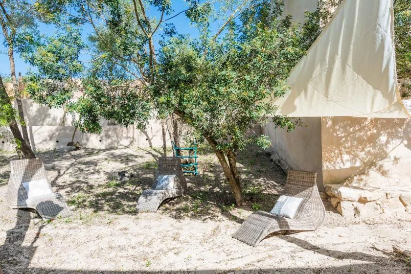 Una zona exterior de descanso a la sombra, con tumbonas tejidas bajo árboles frondosos.