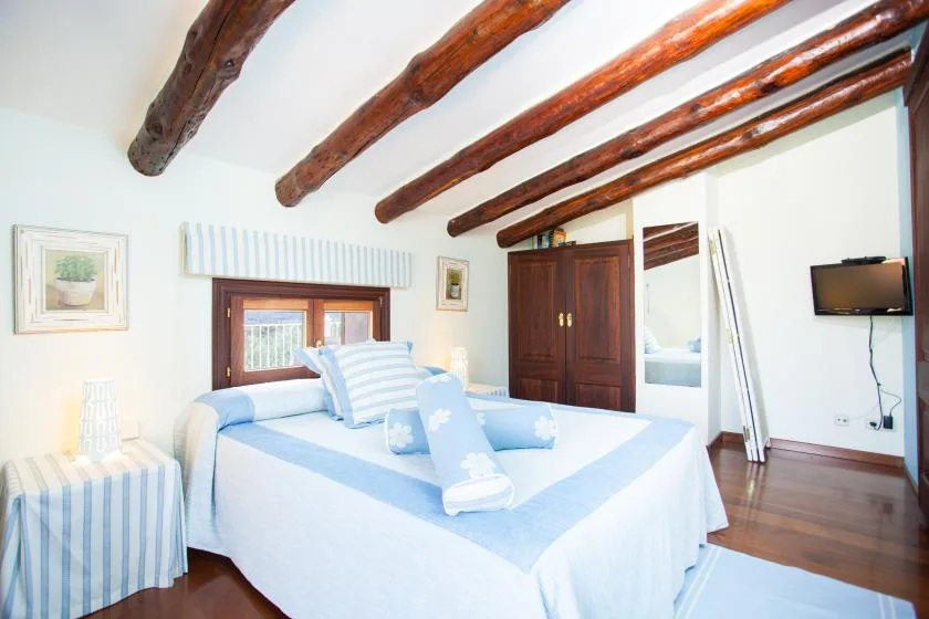 Un dormitorio luminoso con una cama bien hecha bajo vigas de madera expuestas.