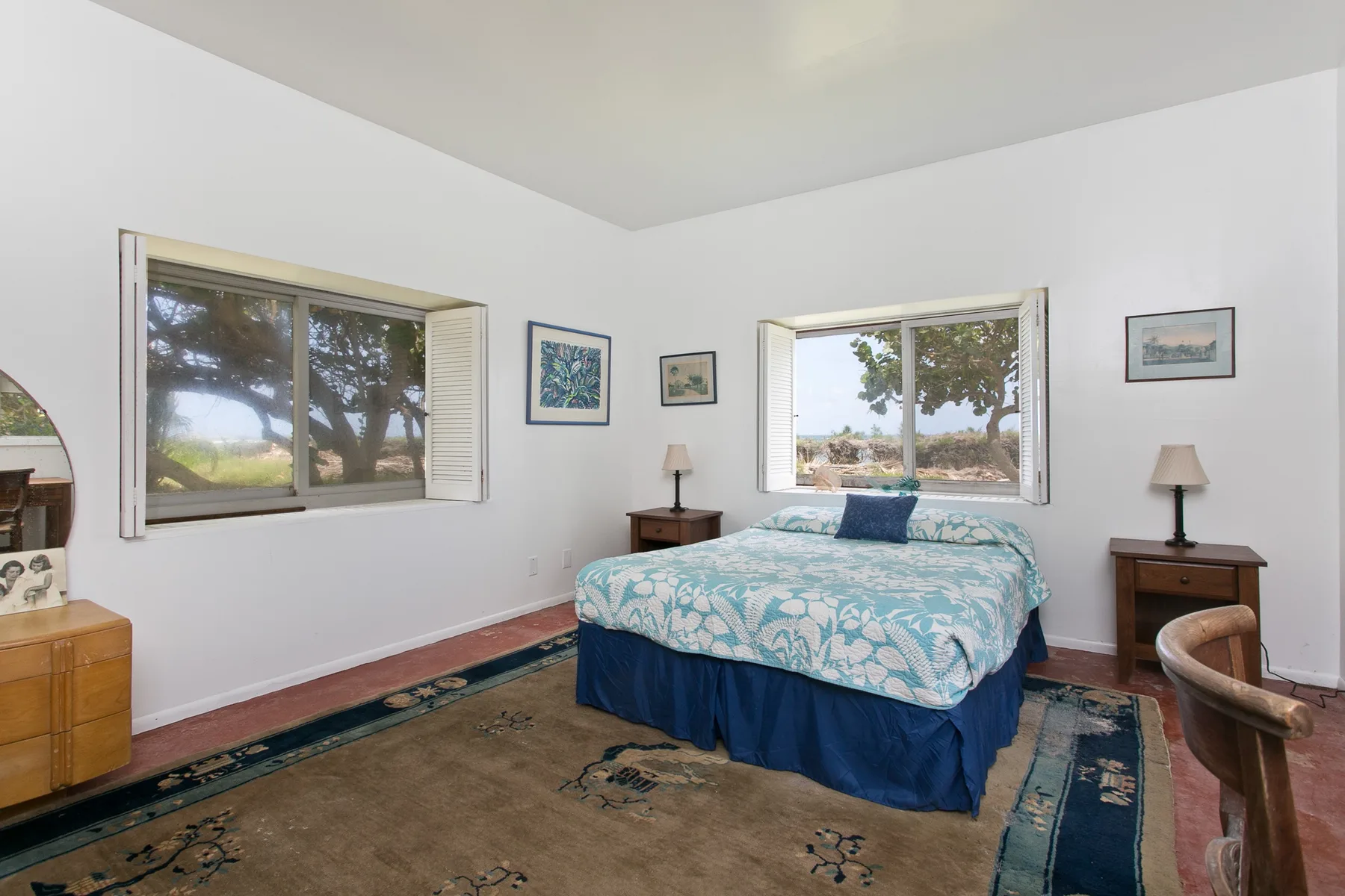 A bedroom with a bed between two windows and bedside tables.