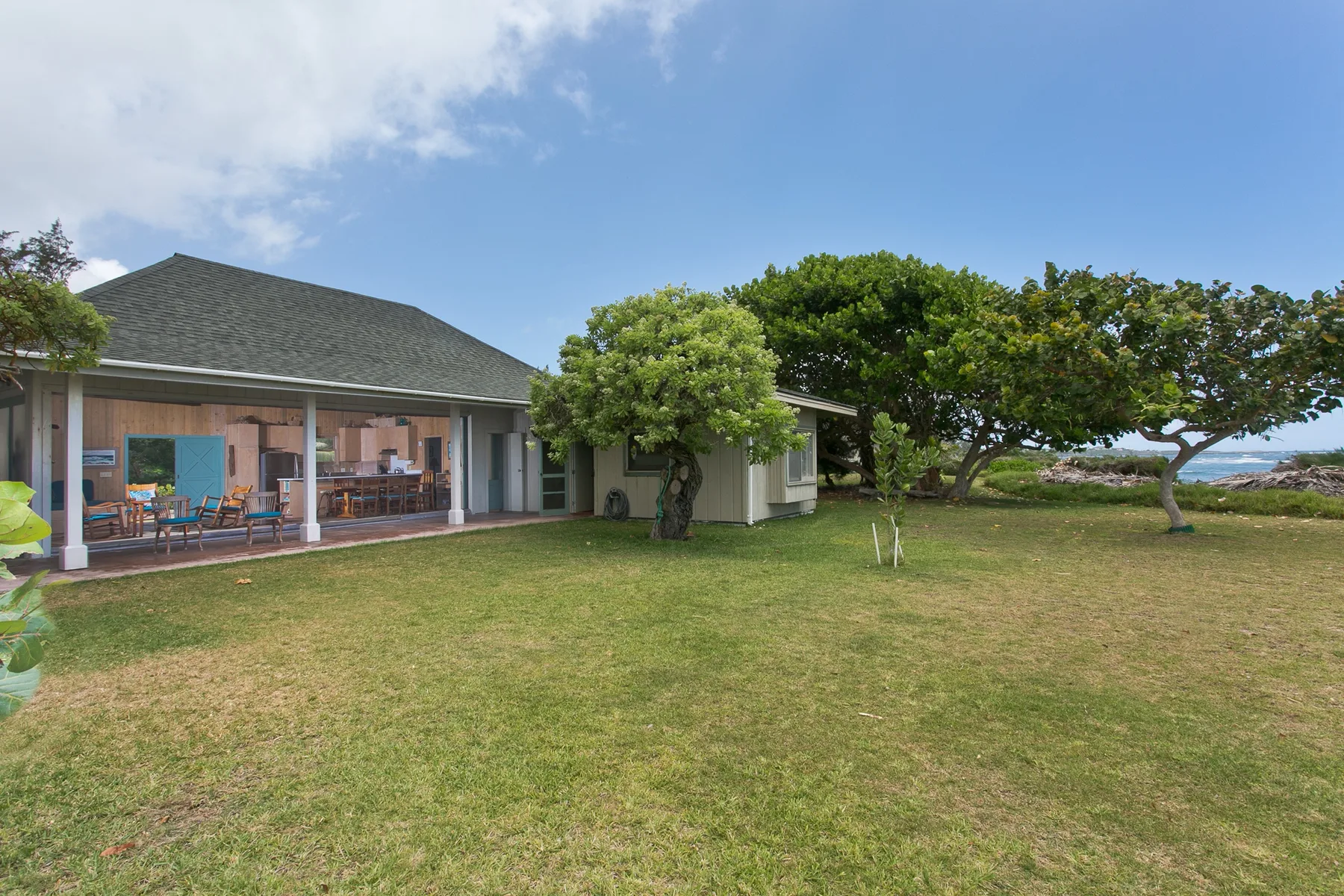 A house with a broad grassy yard, mature trees, and a covered patio.