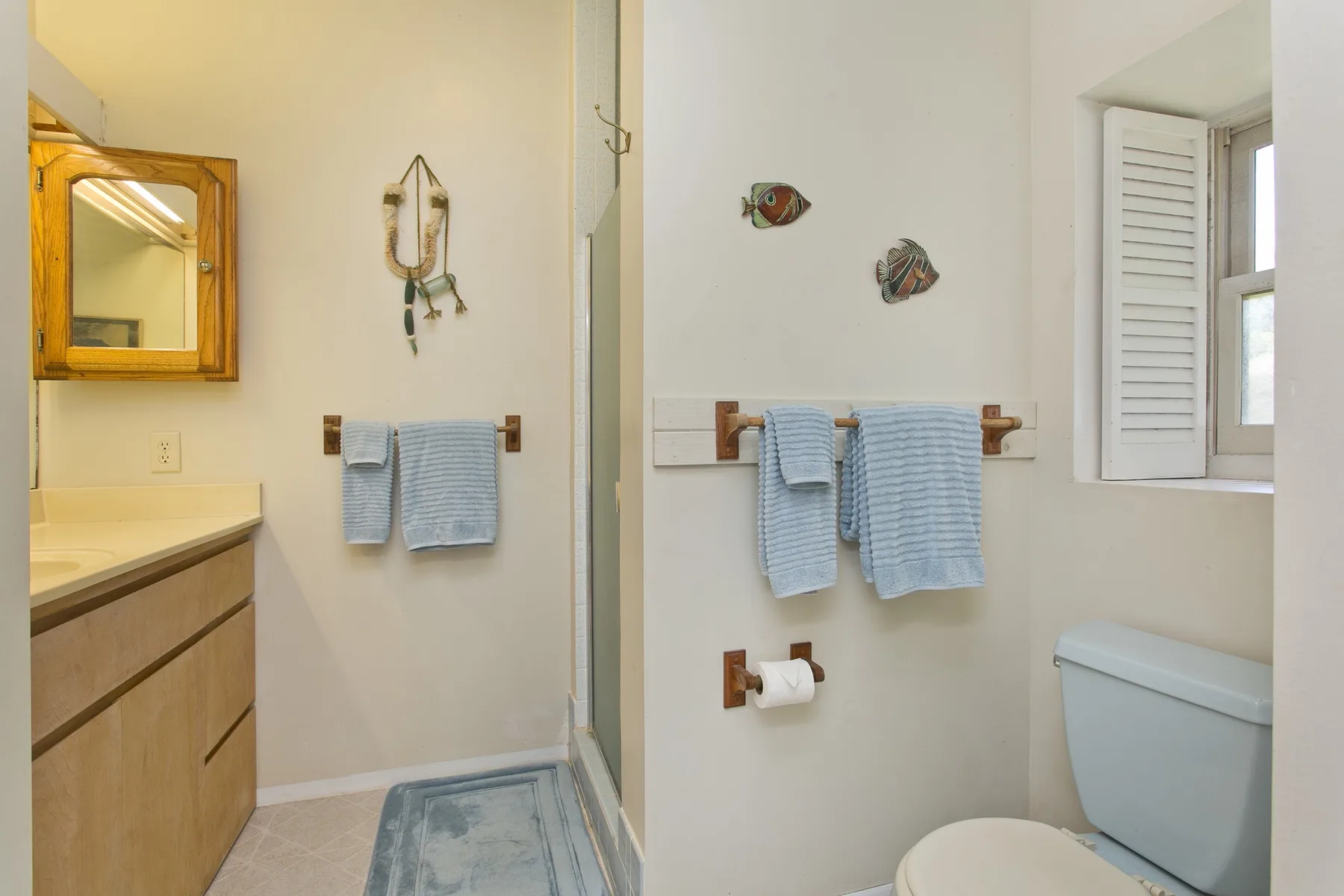 A bathroom with a sink, towel bars, and a toilet beside a window.
