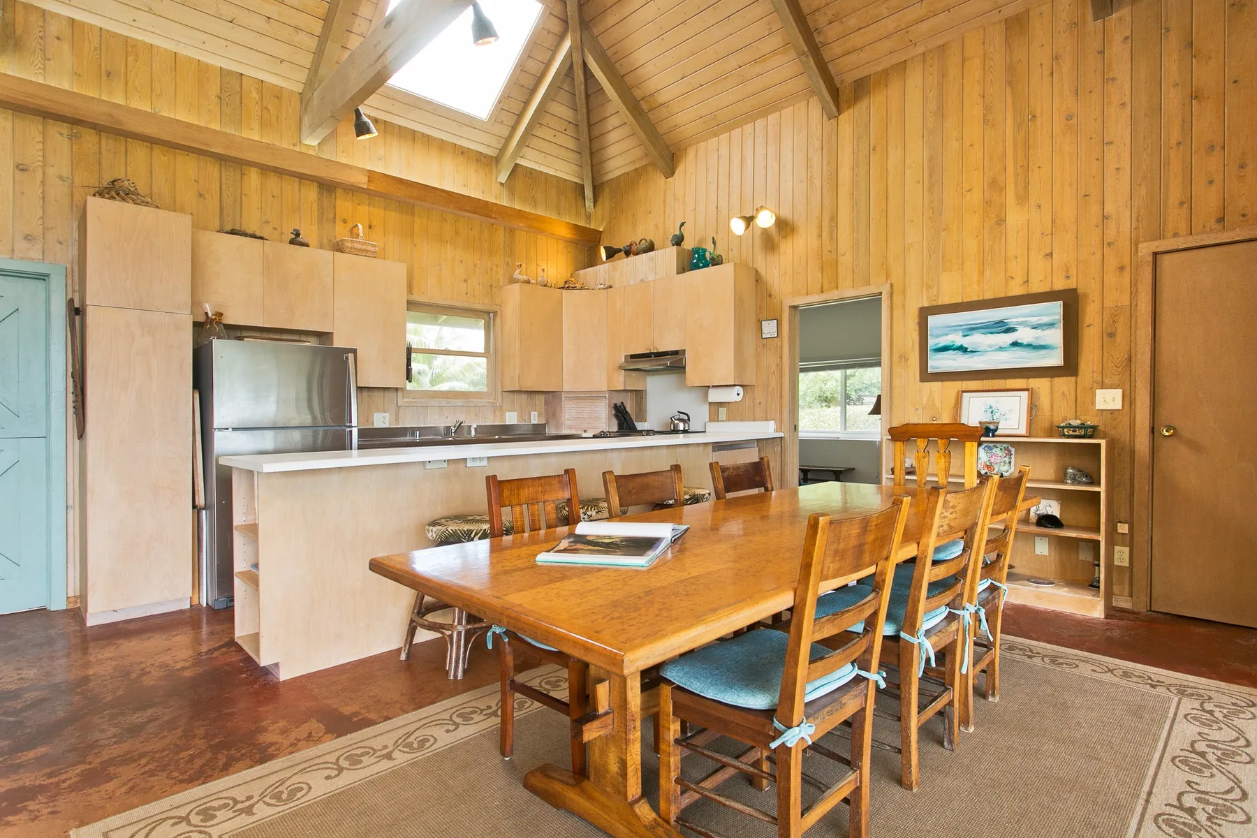 A wood-paneled dining area with a long table beside an open kitchen.