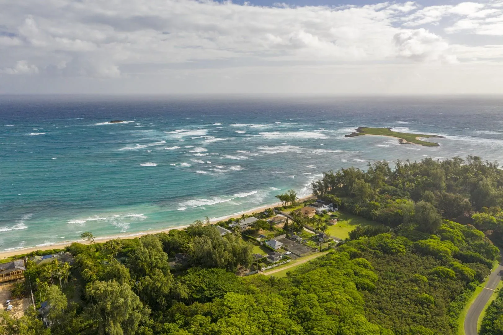 Aerial view of a green coastal landscape beside a turquoise ocean.