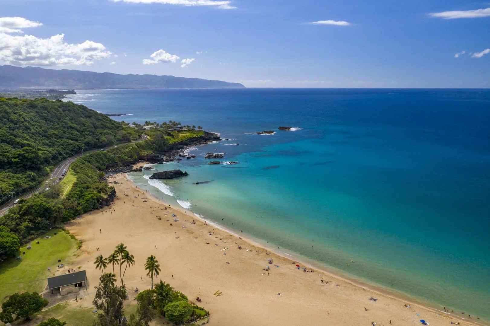 Aerial view of a sandy beach and turquoise ocean beside a green coastline.