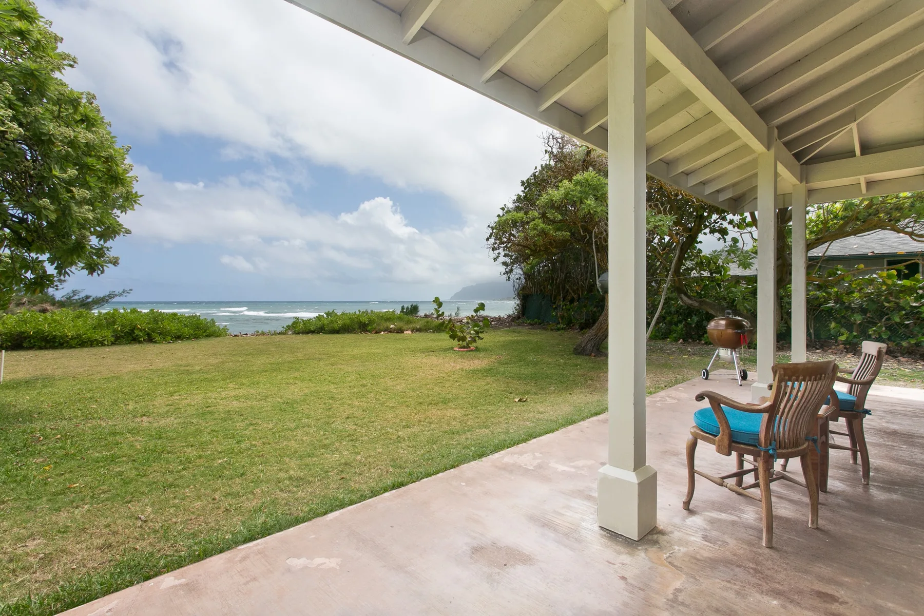 A covered patio with seating overlooks a grassy yard and the ocean.