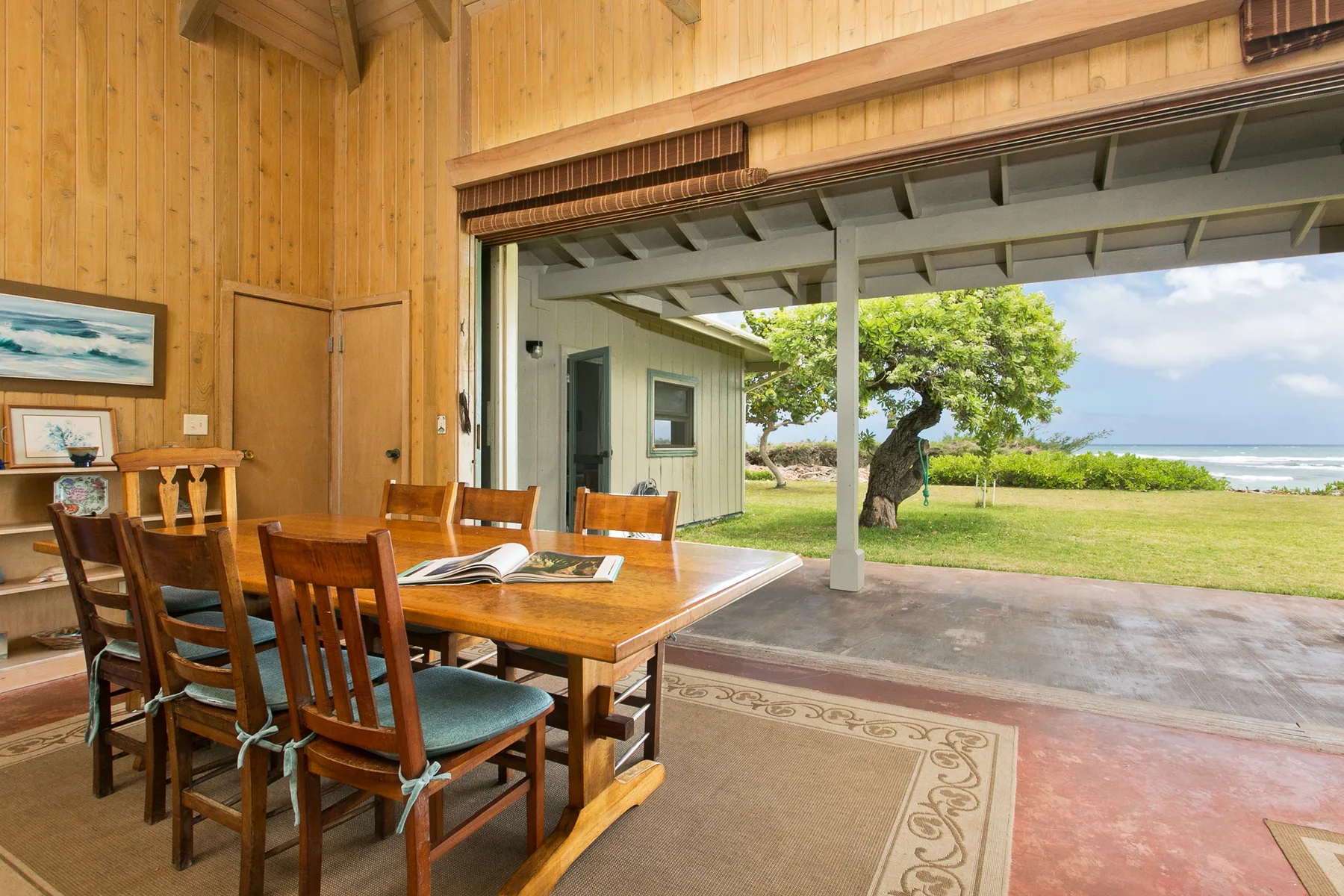A wood-paneled dining area opens onto a covered patio and grassy seaside view.