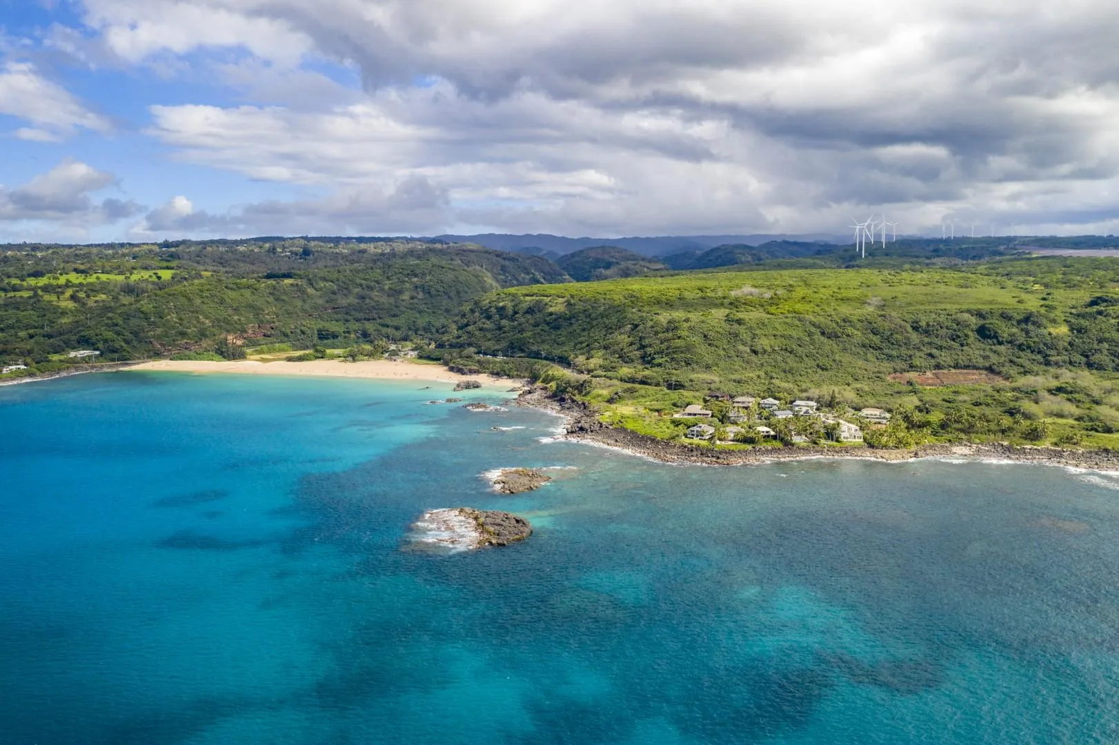 Aerial view of a turquoise bay with a sandy beach and green hills.
