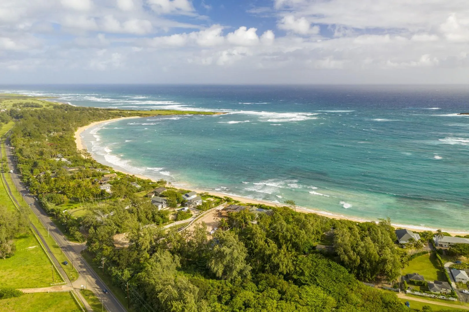 Aerial view of a curving beach, turquoise water, and green coastal vegetation.