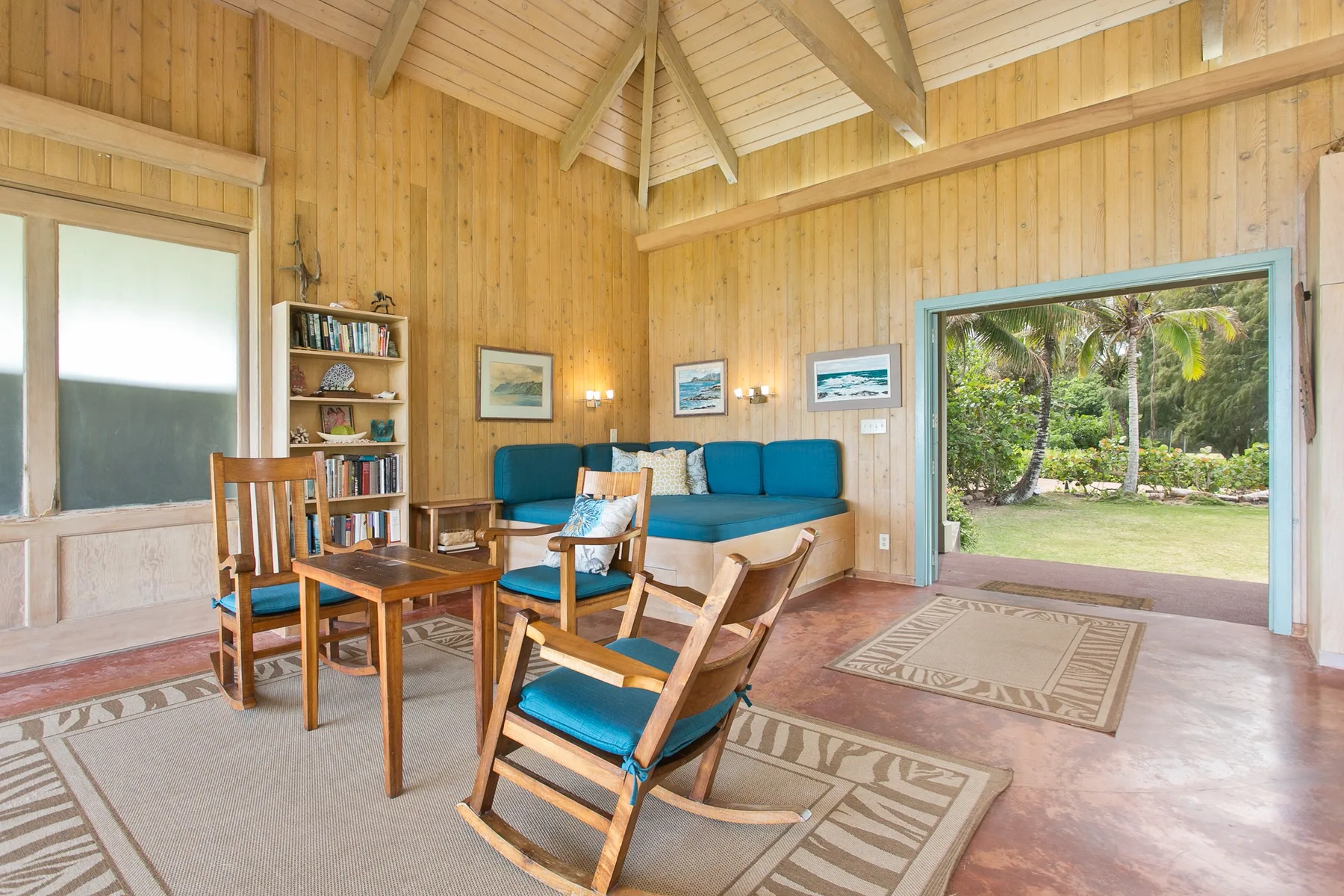 A wood-paneled sitting room with blue seating and a view through the open doorway to greenery.