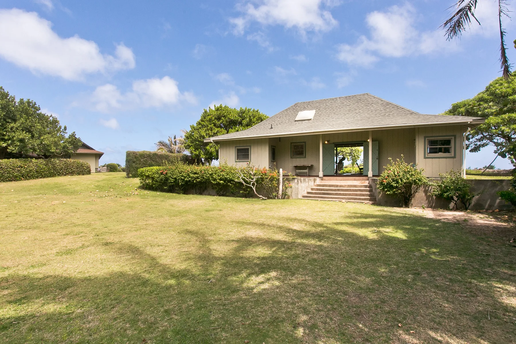 A single-story house sits beyond a broad grassy lawn, with shrubs along the front.