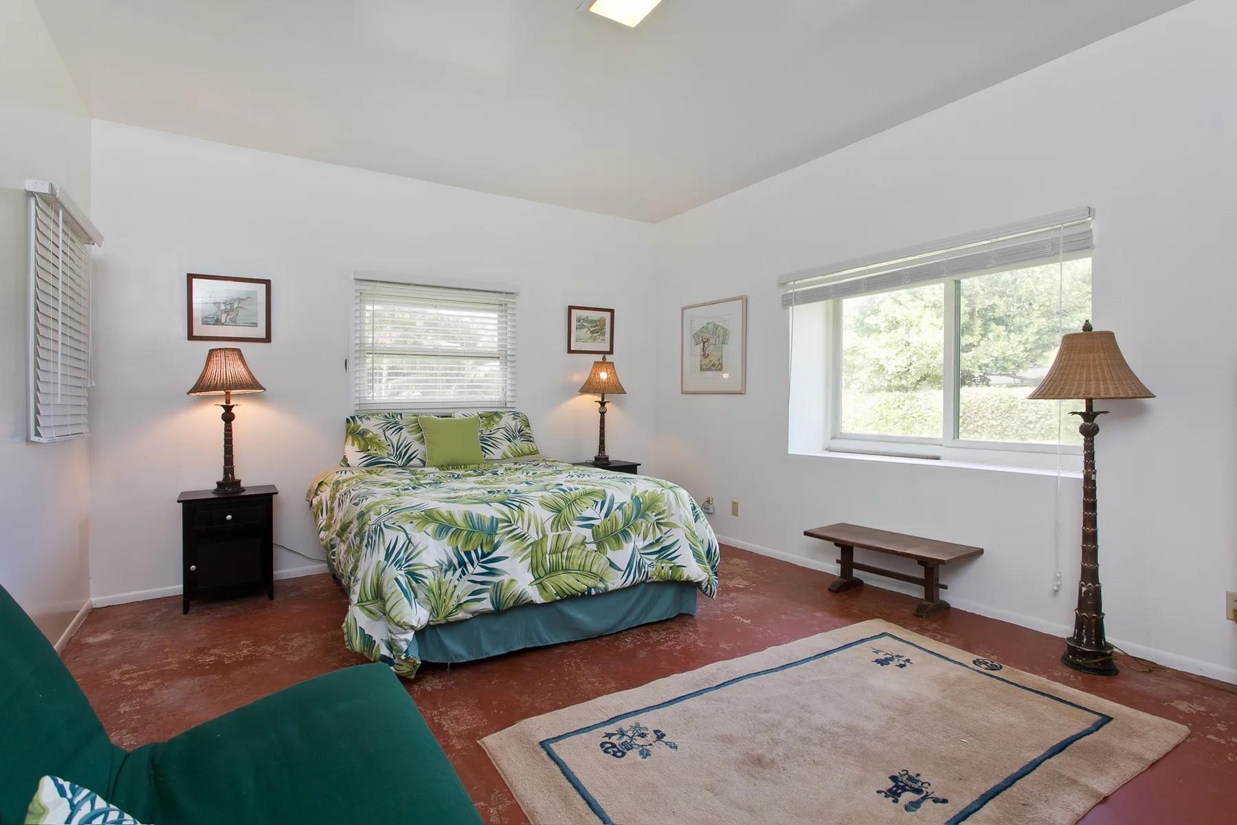 A bedroom with a bed covered in a leafy pattern and a rug.