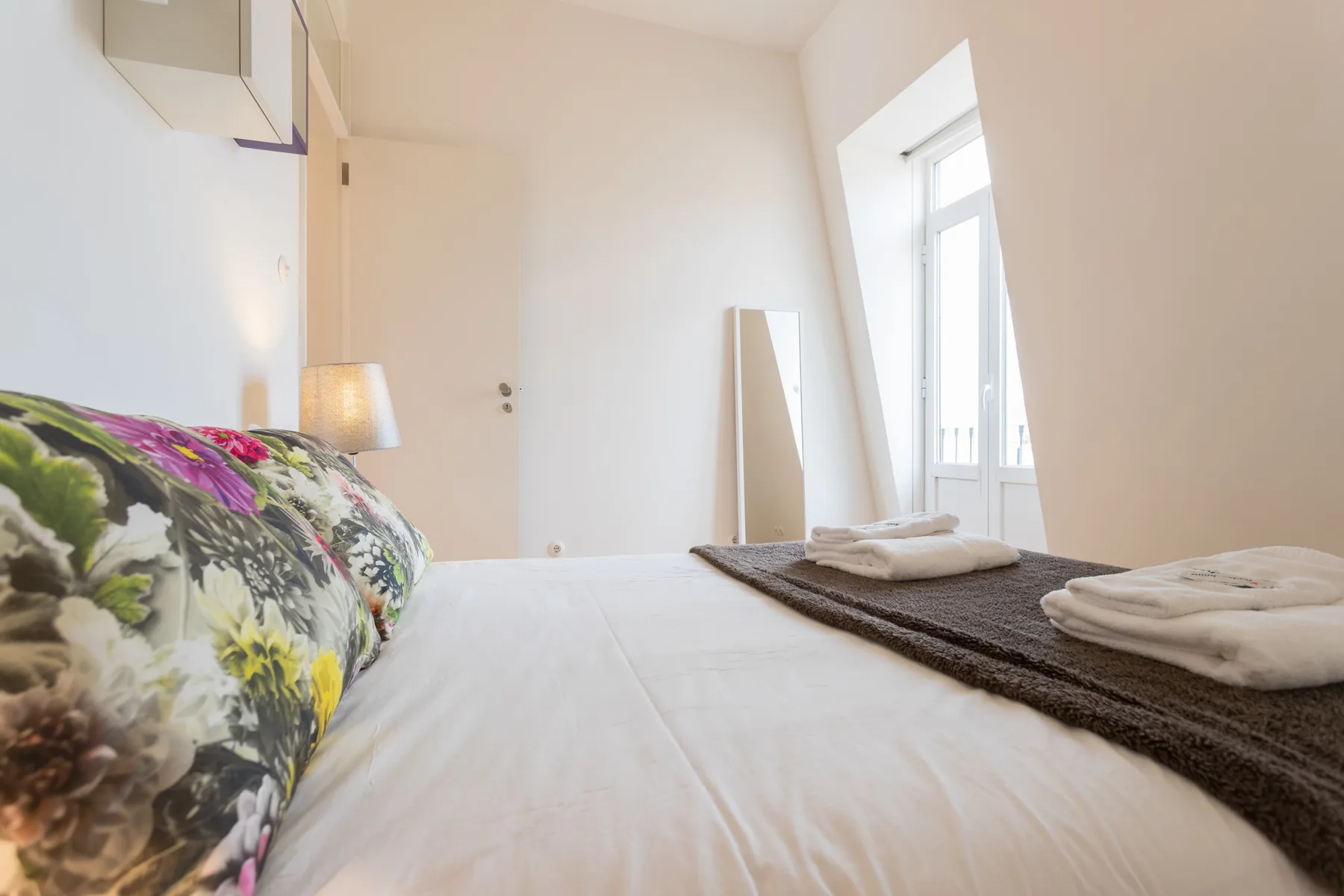 Un dormitorio luminoso con una colcha floral y toallas dobladas junto a la ventana.