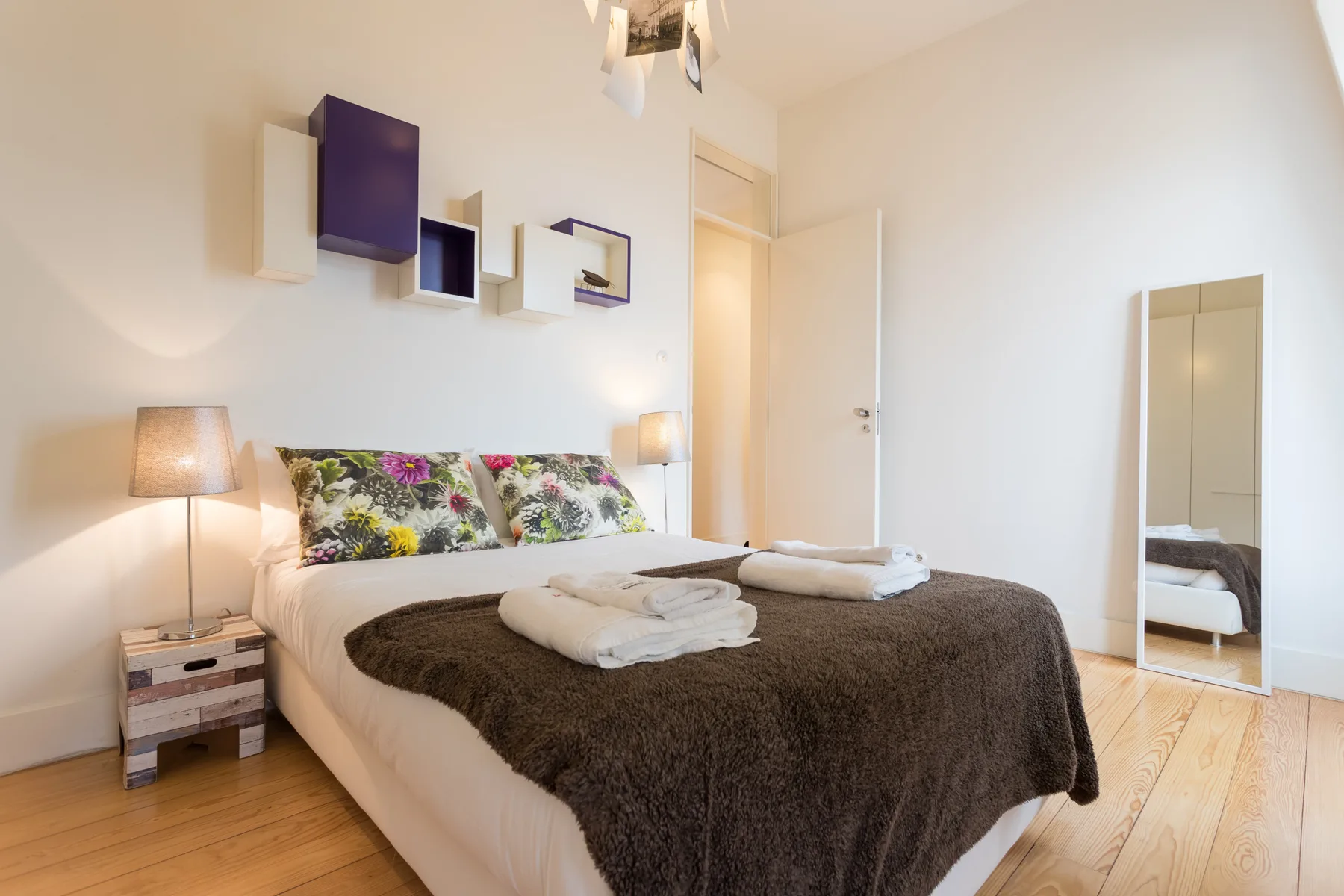 Un dormitorio con cama doble, almohadas estampadas y un espejo de cuerpo entero.