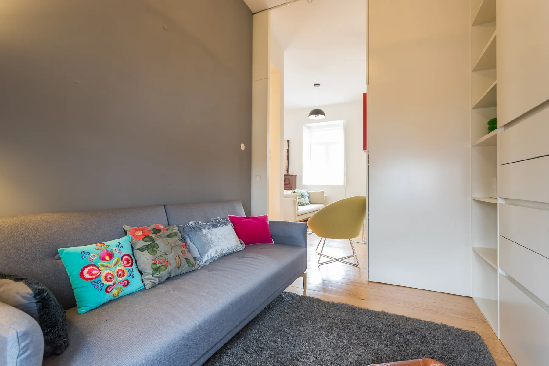 Sala de estar con sofá gris, cojines coloridos y estanterías empotradas.