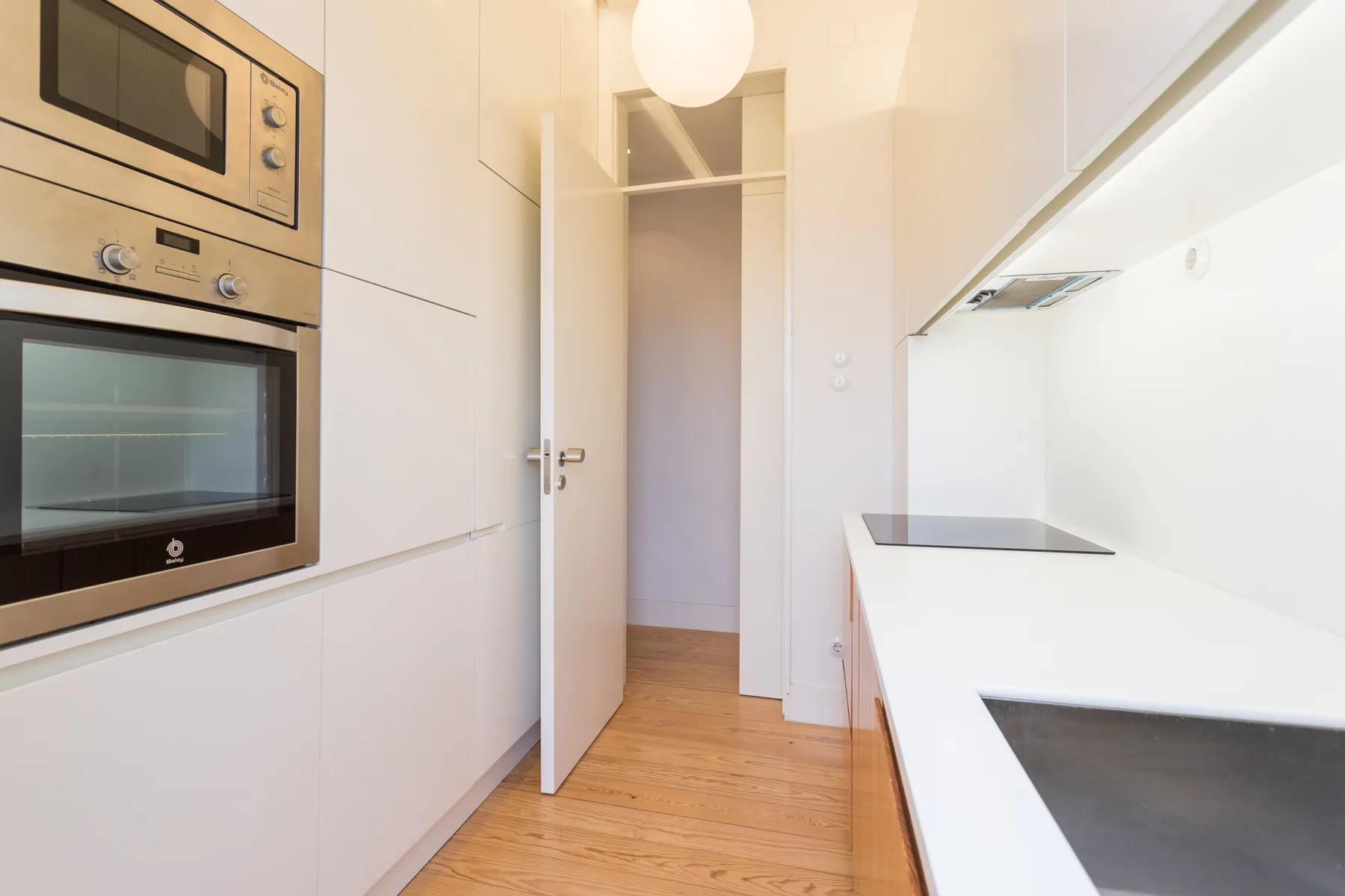 Una cocina estrecha con electrodomésticos empotrados, gabinetes blancos y una puerta.