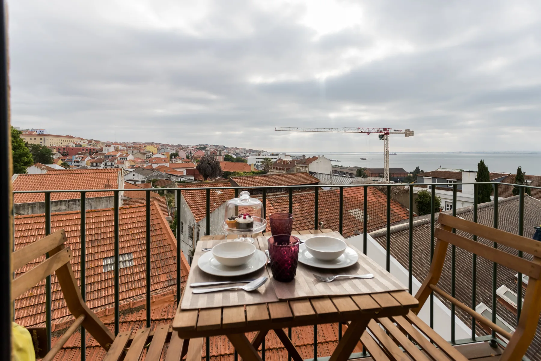 Una zona de comedor en un balcón da a tejados y un horizonte urbano lejano.