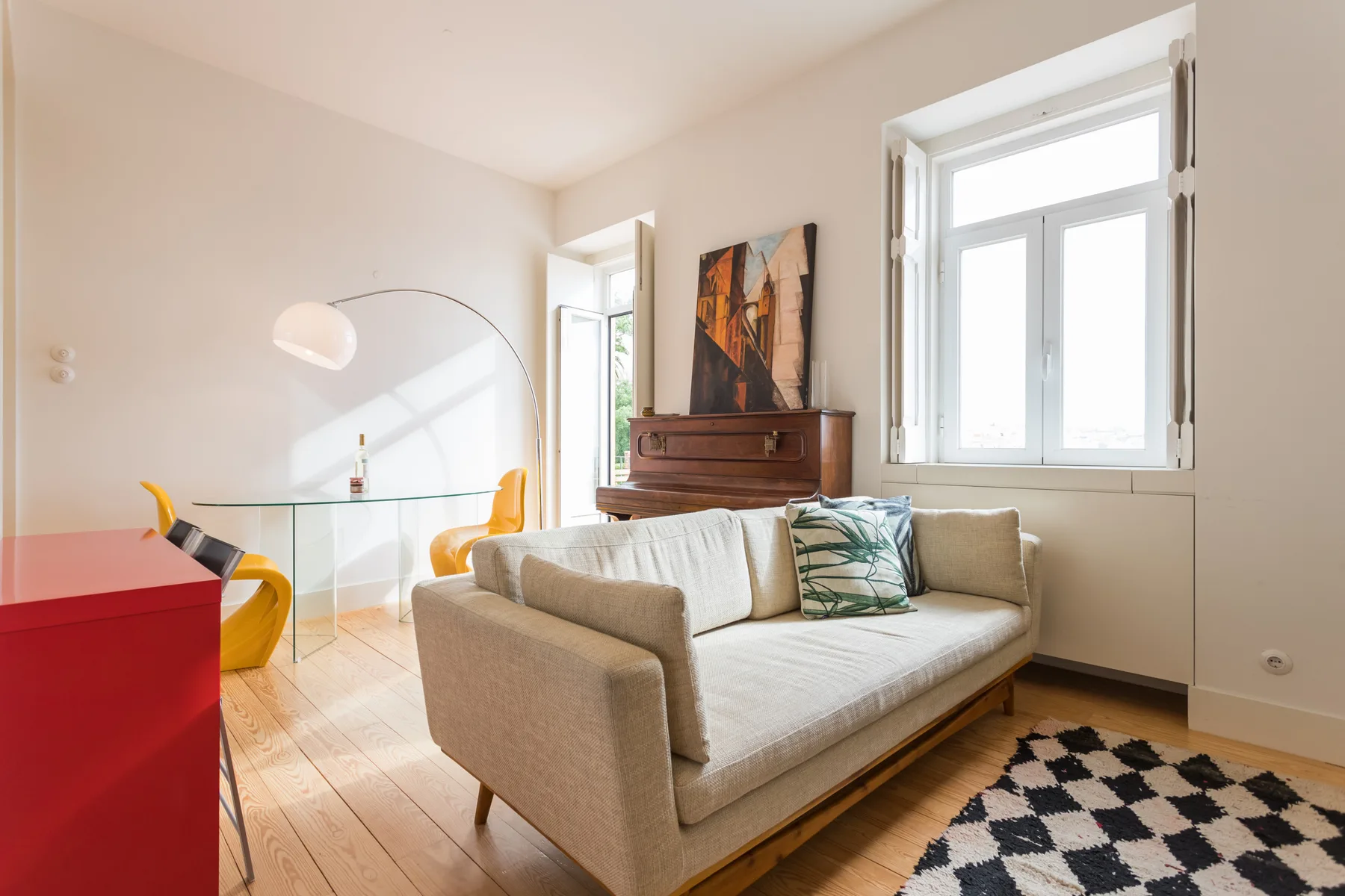 Una sala luminosa con un sofá claro y ventanas grandes.