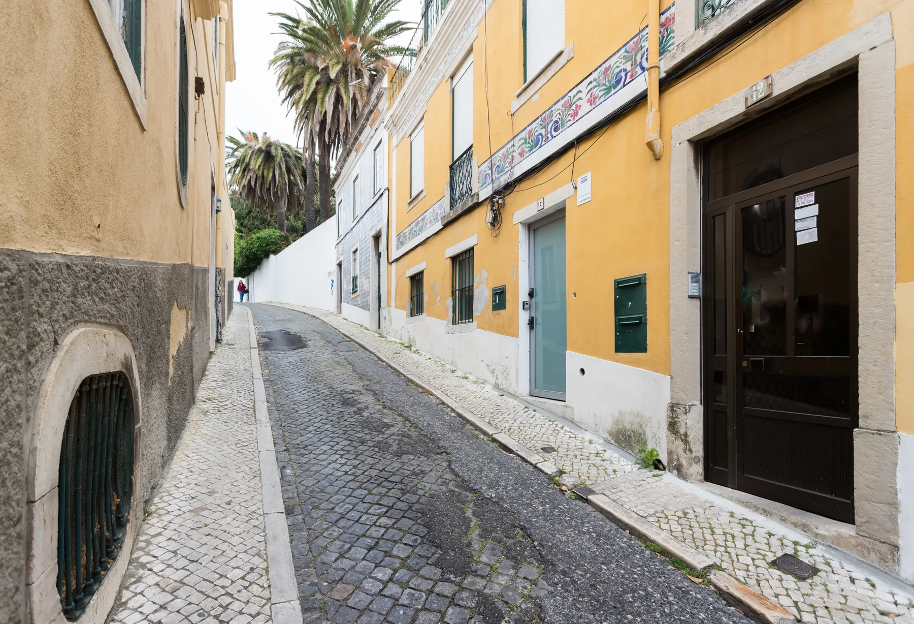 Una calle estrecha empedrada pasa entre edificios coloridos, con palmeras al fondo.