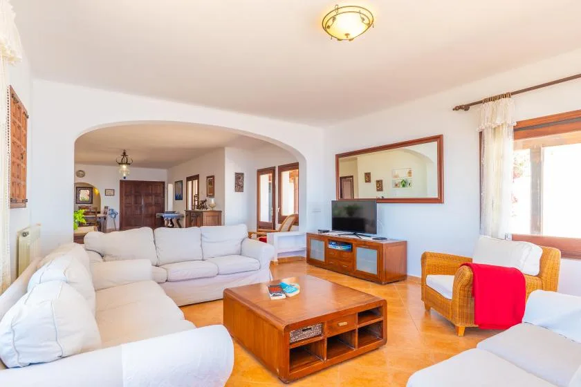 Una sala luminosa con asientos blancos, una mesa de centro de madera y un televisor.