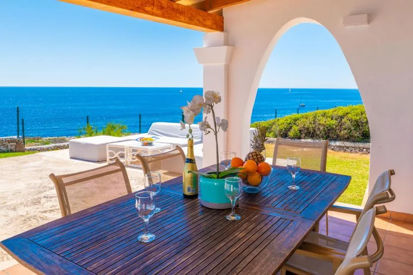 Una zona de comedor al aire libre da al mar, con una mesa de madera bajo un arco.