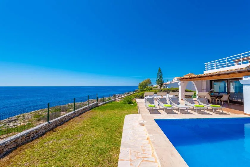 Una terraza con piscina y tumbonas junto al mar.