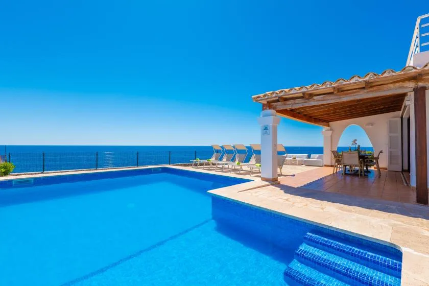 Una piscina junto a un patio cubierto con vistas al mar.
