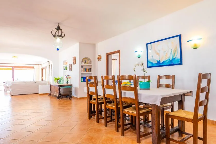 Un comedor con una mesa larga y asientos de madera junto a una luminosa sala de estar.