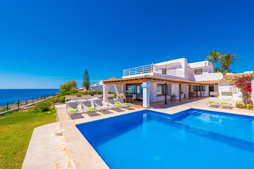 Una casa junto al mar con piscina y asientos de descanso tiene vistas al océano.