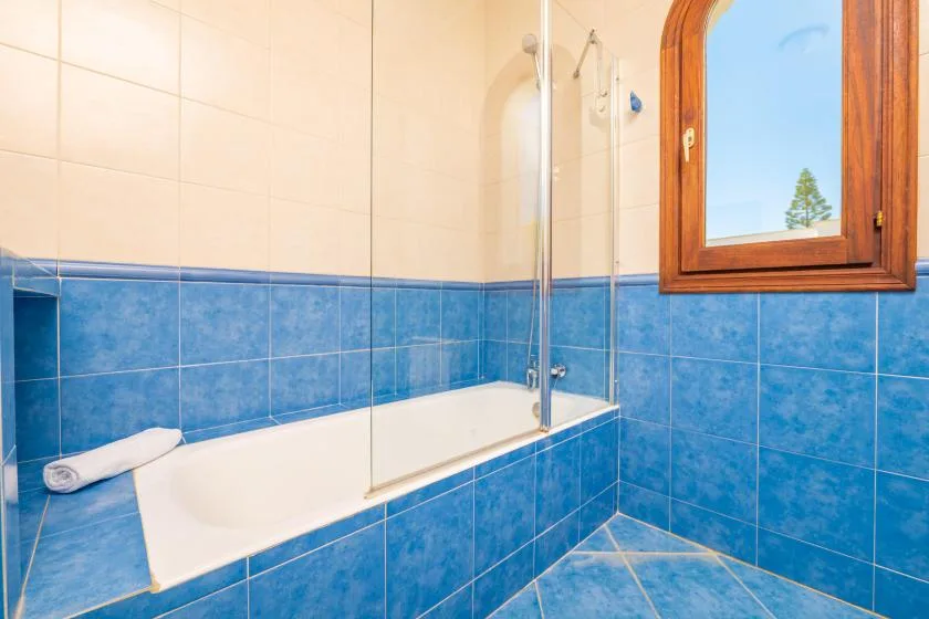 Un baño alicatado con bañera, ducha y una ventana con marco de madera.