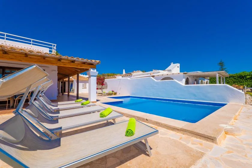 Una piscina al aire libre junto a un patio sombreado con tumbonas reclinables.