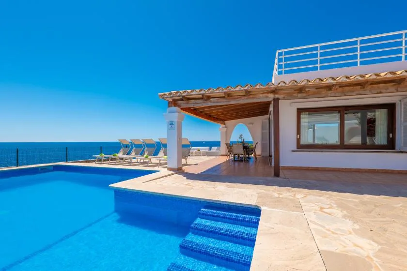 Patio junto al mar con piscina y una zona de asientos a la sombra.