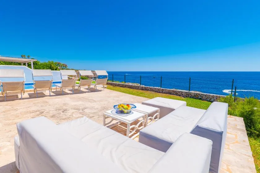 Una terraza junto al mar tiene asientos blancos y vistas al océano azul.