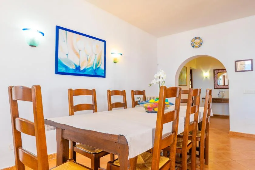 Un comedor con una mesa larga y asientos de madera bajo un cuadro enmarcado.