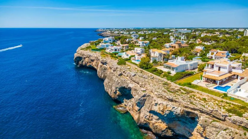 Un barrio costero de casas se extiende junto a una costa rocosa y el mar azul.