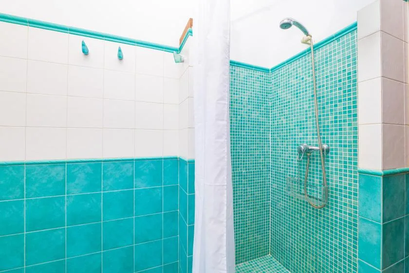 Una ducha de baño alicatada con cortina blanca y cabezal fijado a la pared.