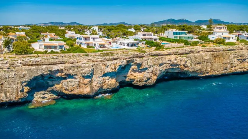 Un acantilado rocoso da al mar de aguas azules, con casas y vegetación en la parte superior.