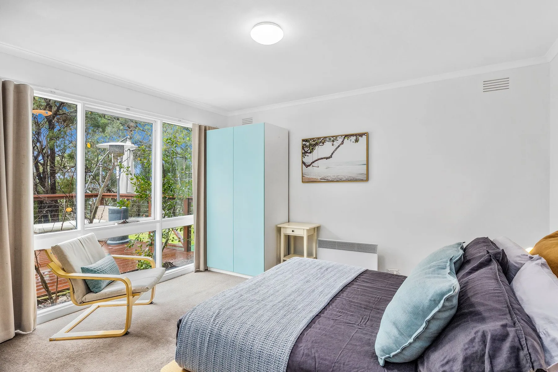 A bedroom with a bed, a chair, and large windows overlooking trees.