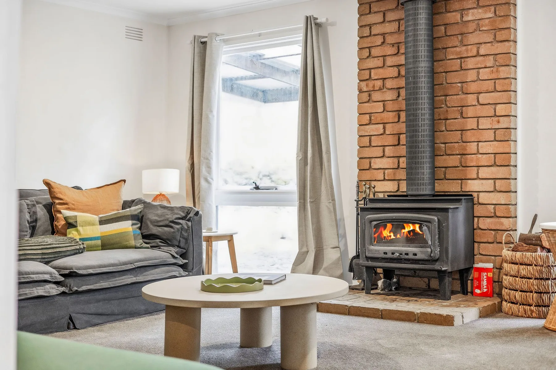 A living room with seating, a coffee table, and a lit wood stove.