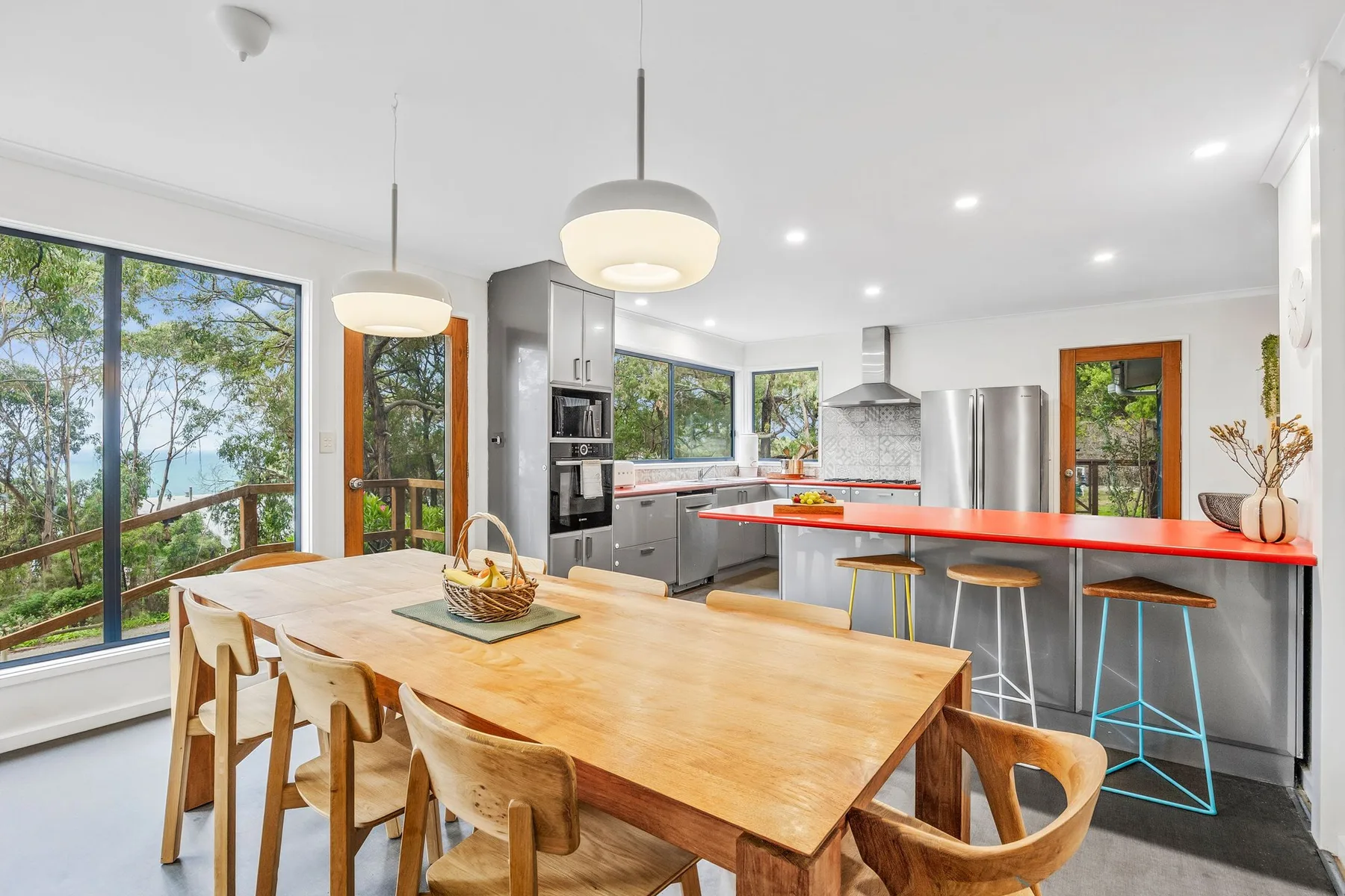 A bright kitchen and dining area with a long wooden table and red countertop.