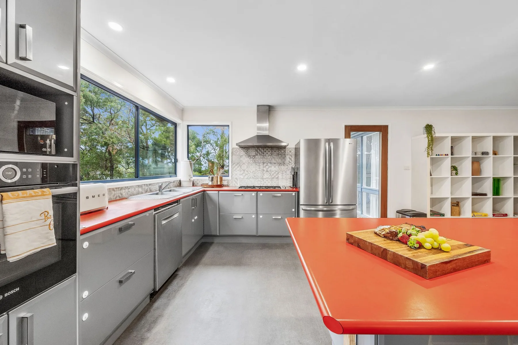 A modern kitchen with gray cabinets, large windows, and a bright orange island.