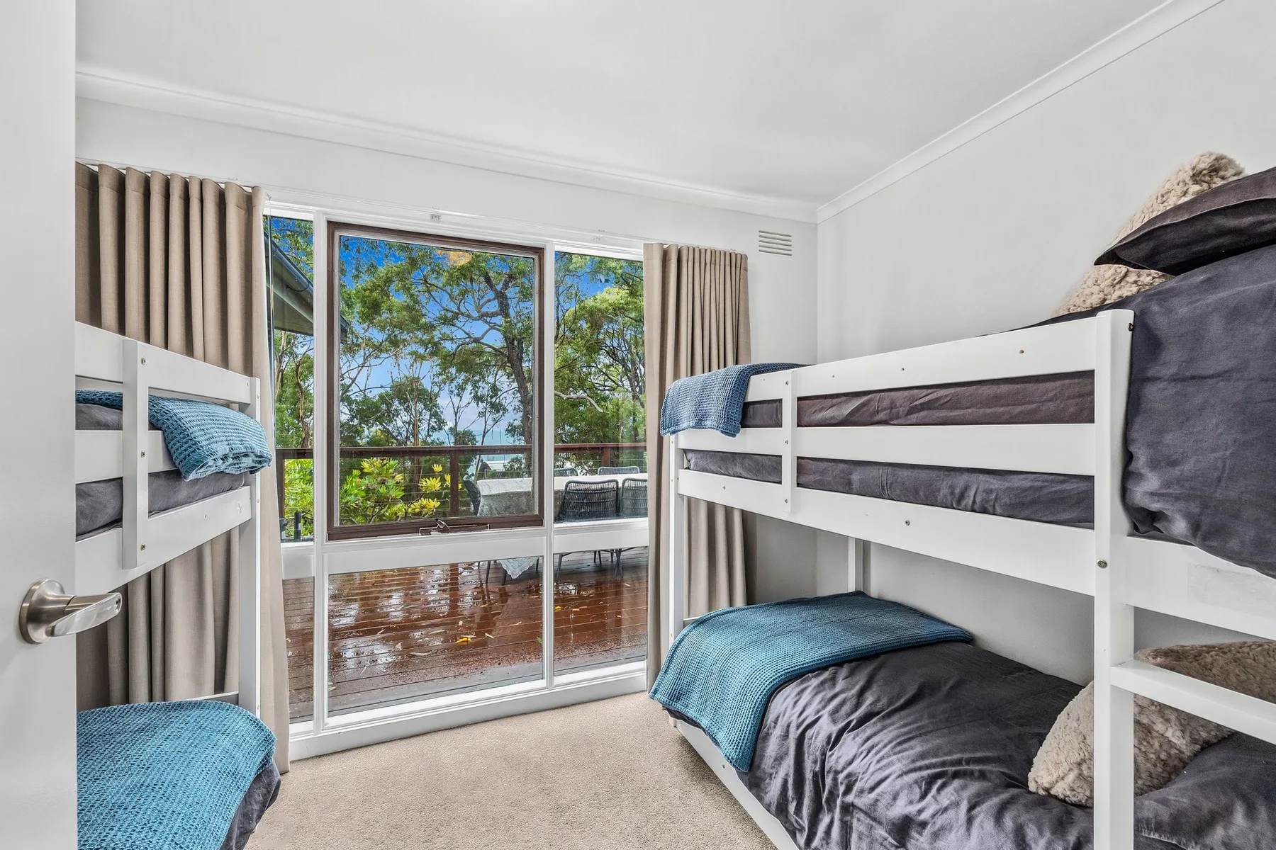 A bright bedroom with bunk beds and sliding glass doors opening onto a balcony.