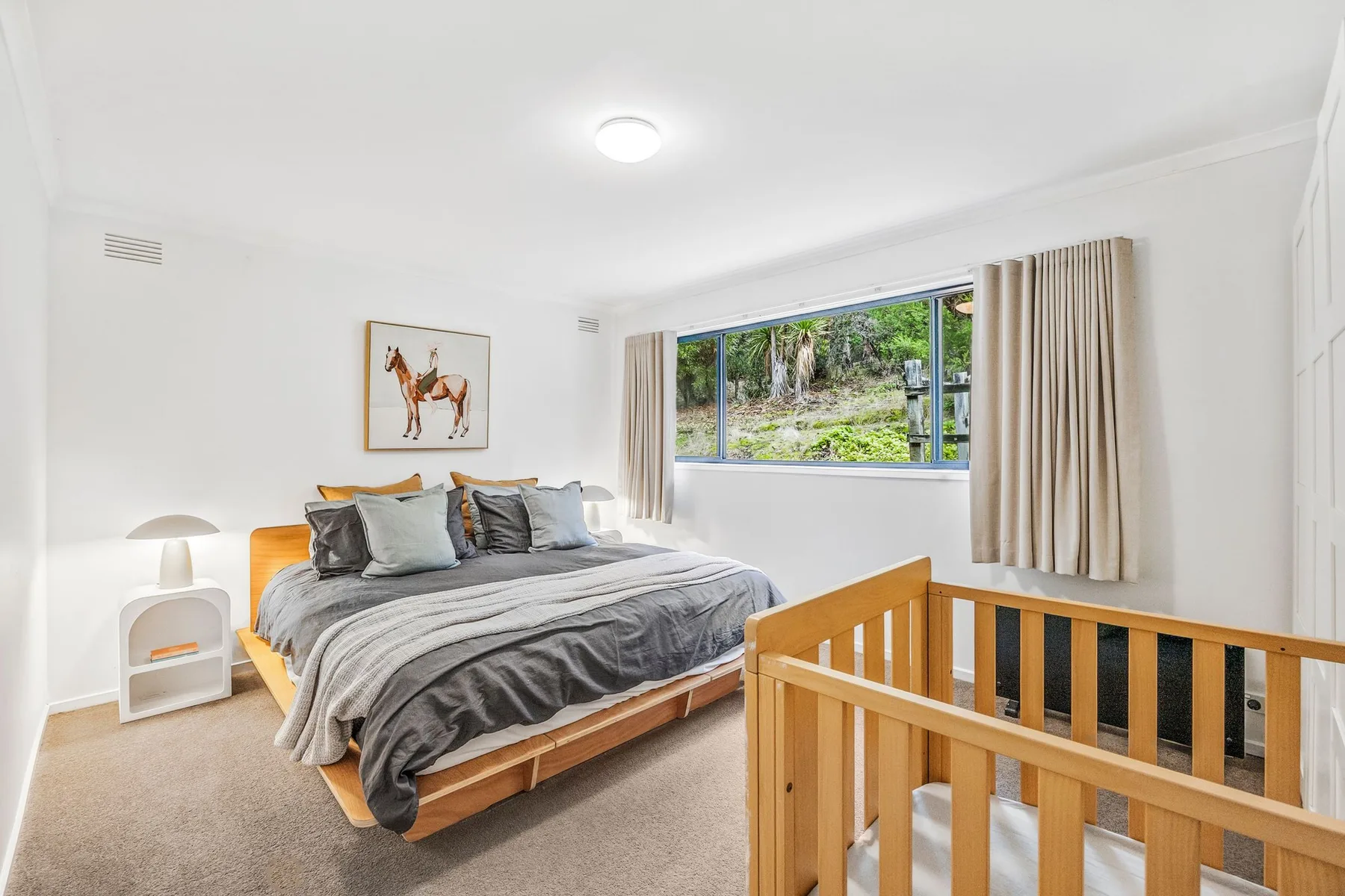 A bedroom with a bed beside a window and a wooden railing.