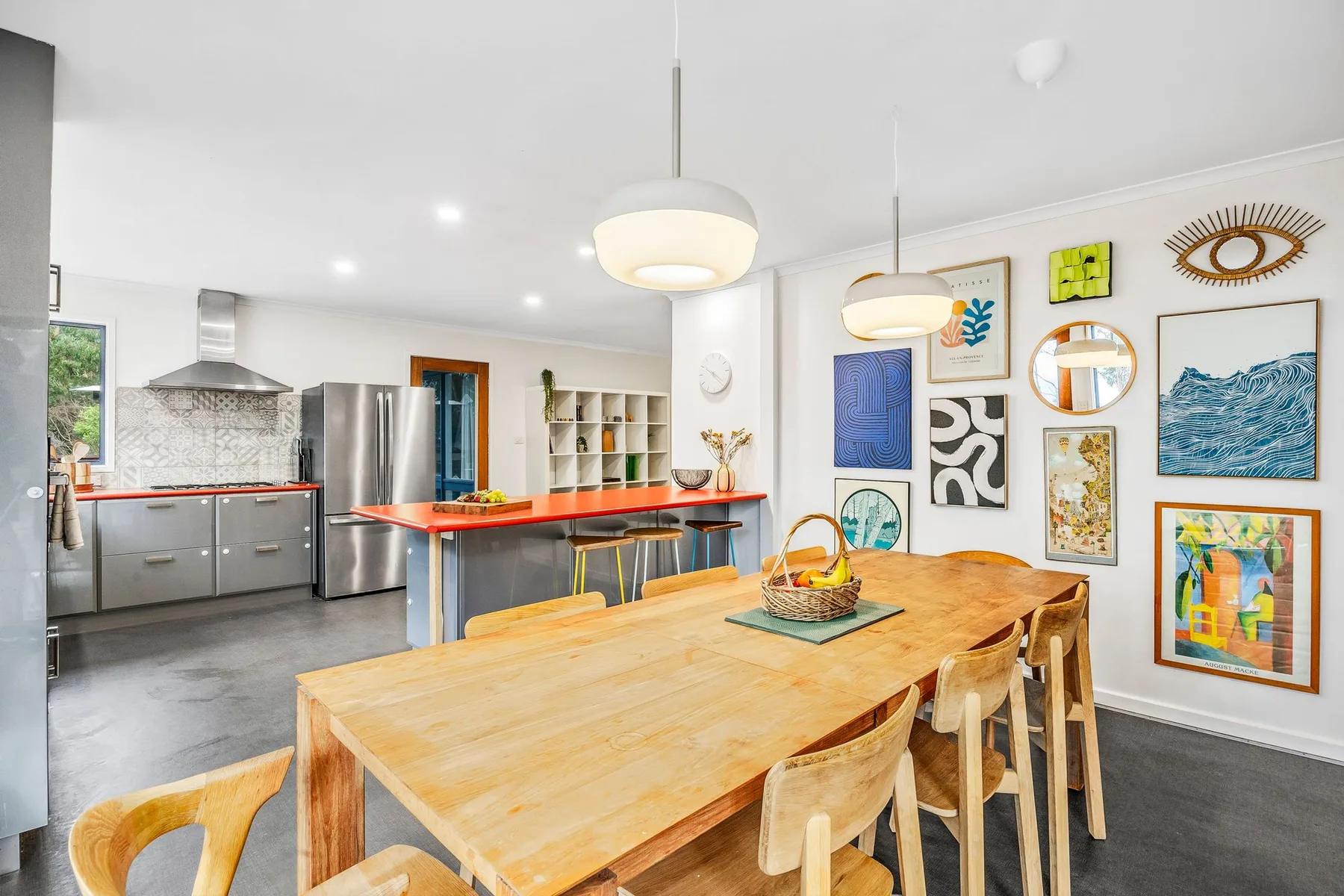 A bright kitchen and dining area with a long wooden table and colorful wall art.