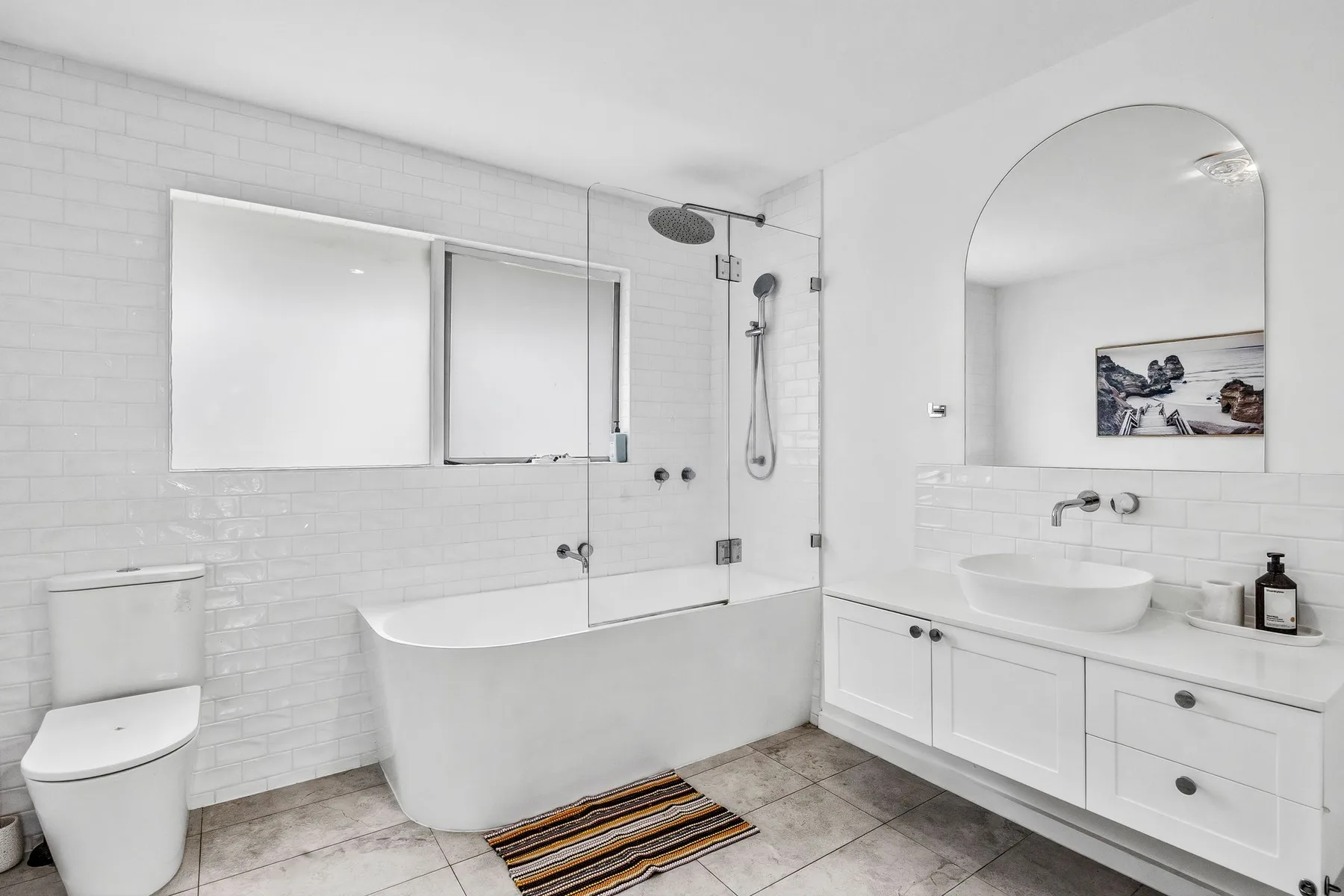 A bright bathroom with a bathtub, shower, and white vanity.