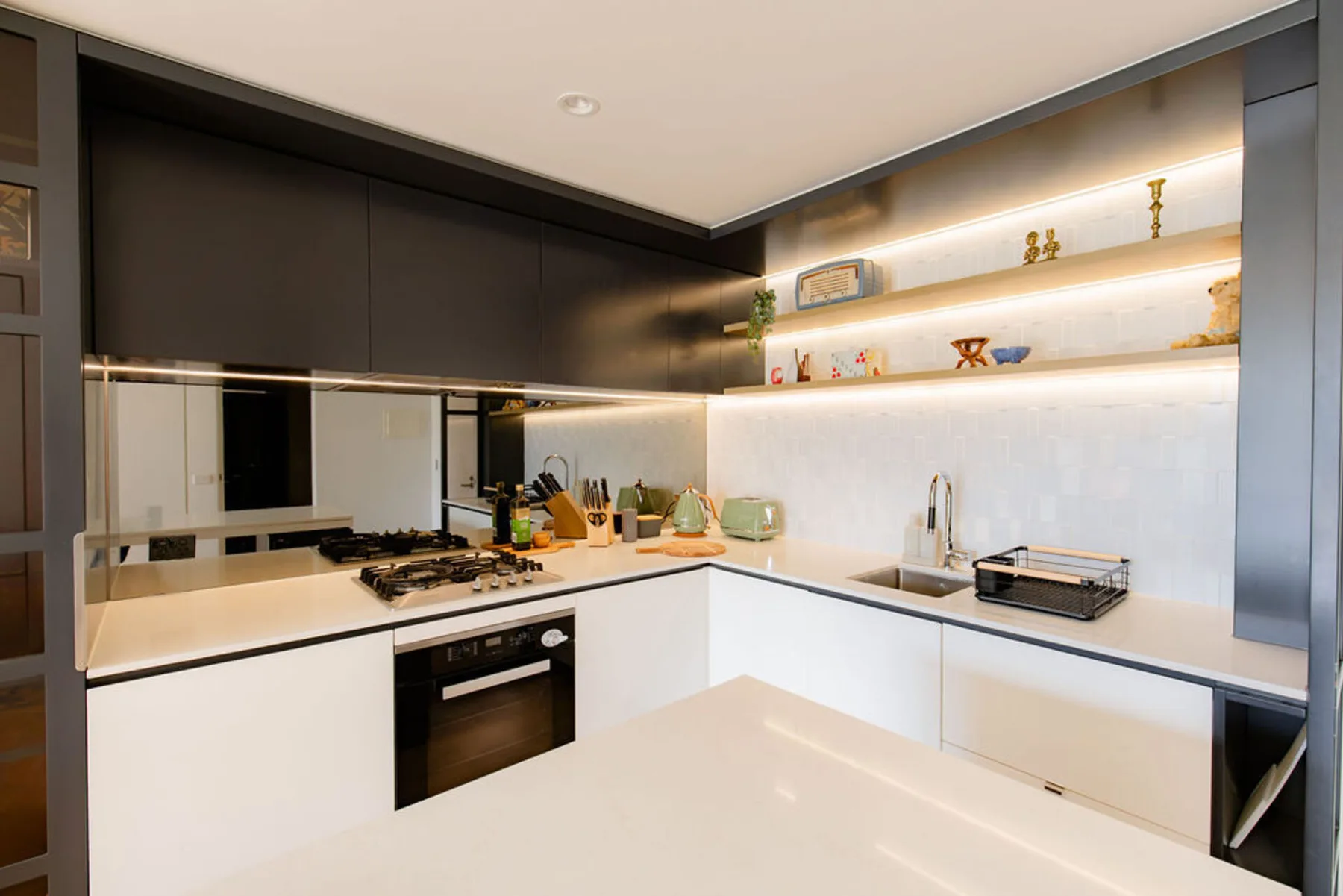 A modern kitchen with a cooktop, oven, and illuminated open shelves.