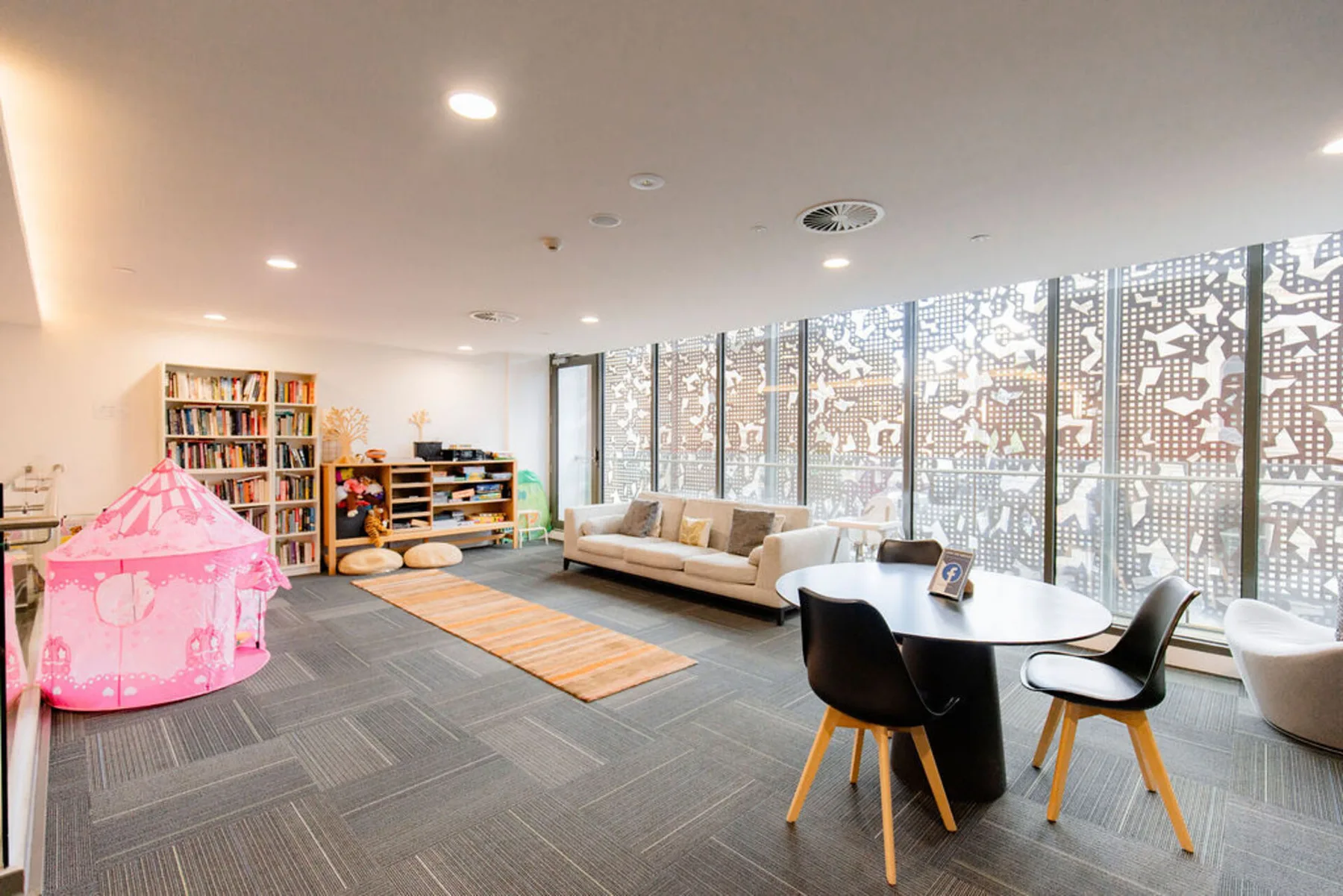 A bright lounge with seating, a round table, and a pink play tent.