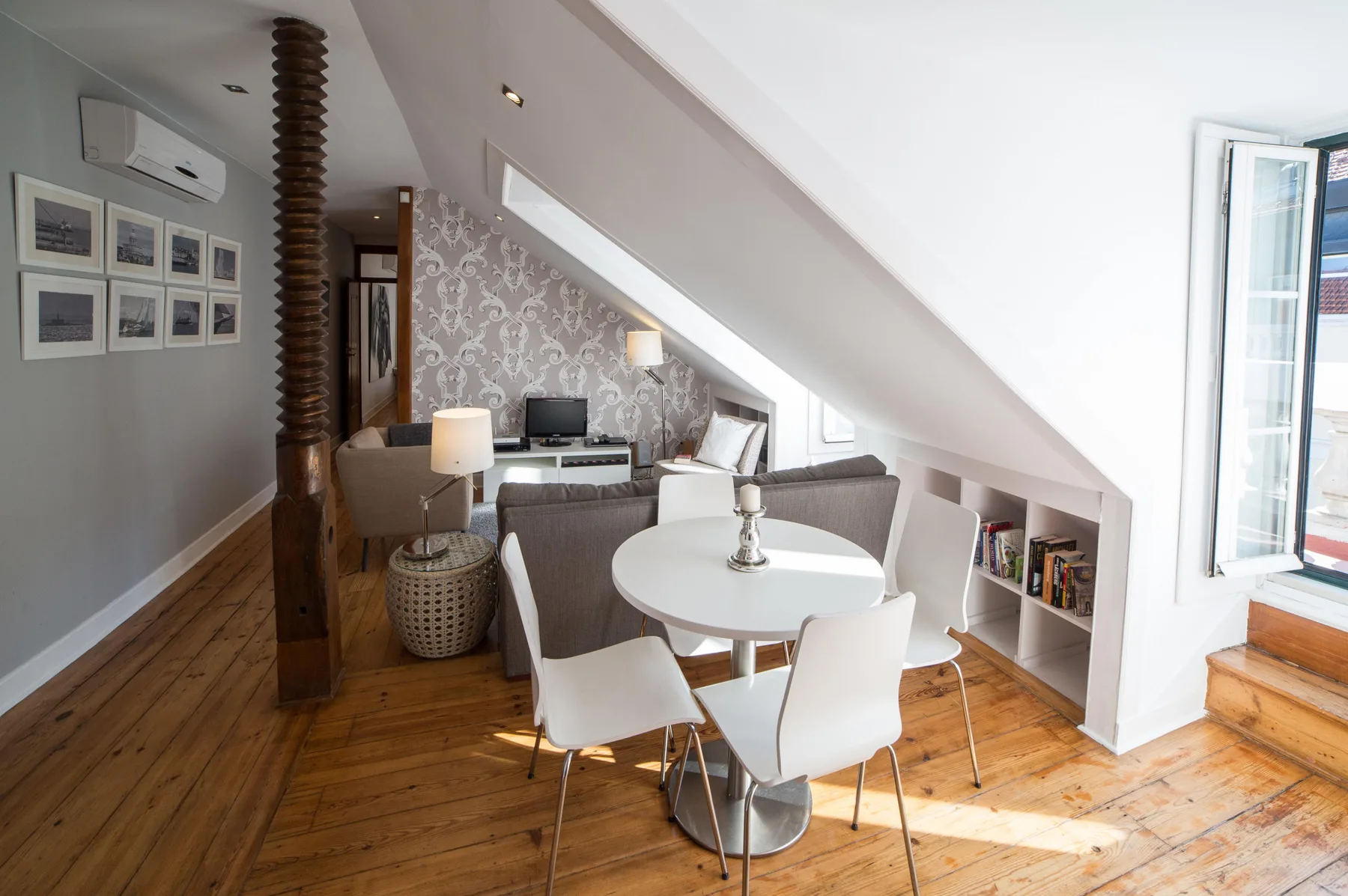 A bright attic living and dining area with seating, a table, and an open window.