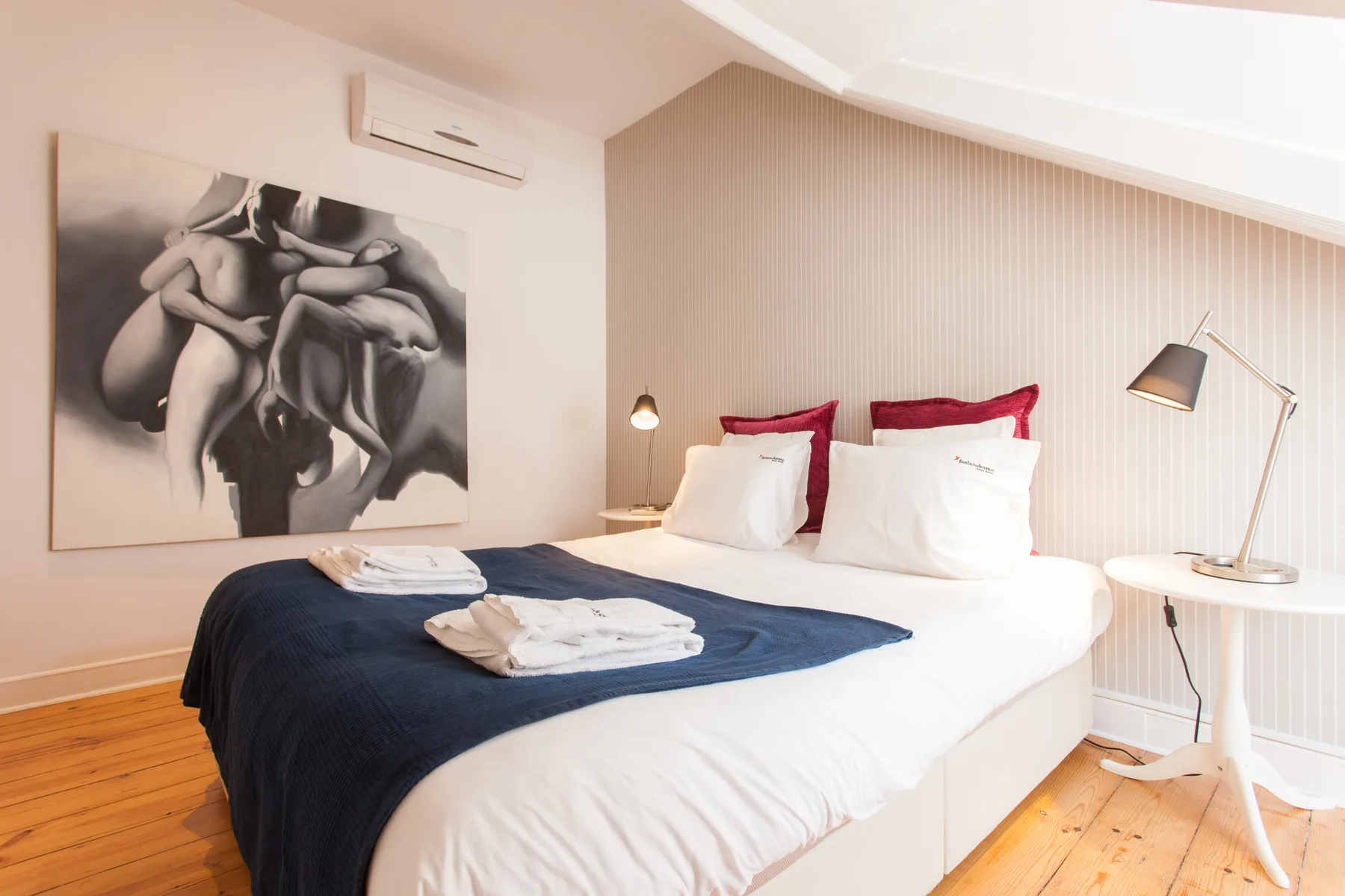 A bedroom with a neatly made bed, wall art, and a bedside lamp.