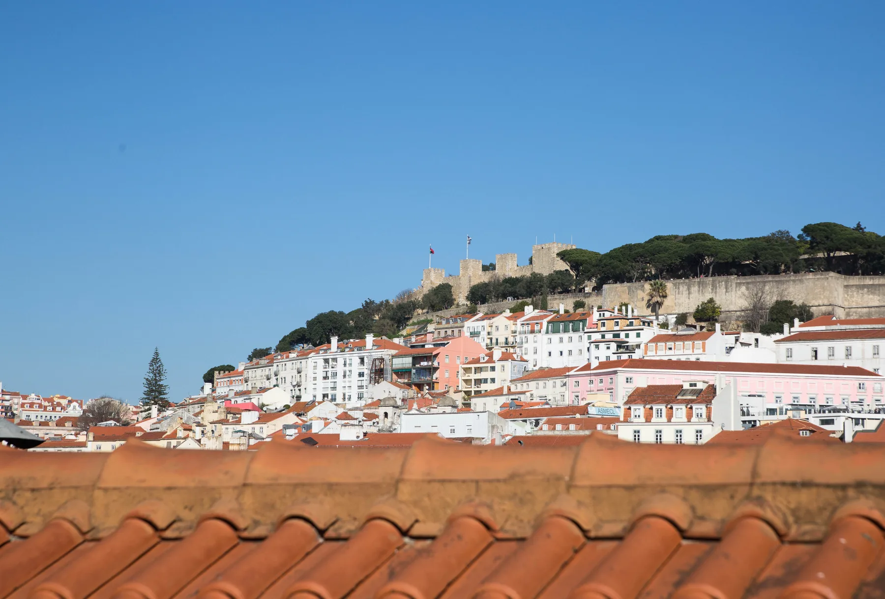 A hillside cityscape with white buildings and a castle above terracotta rooftops.